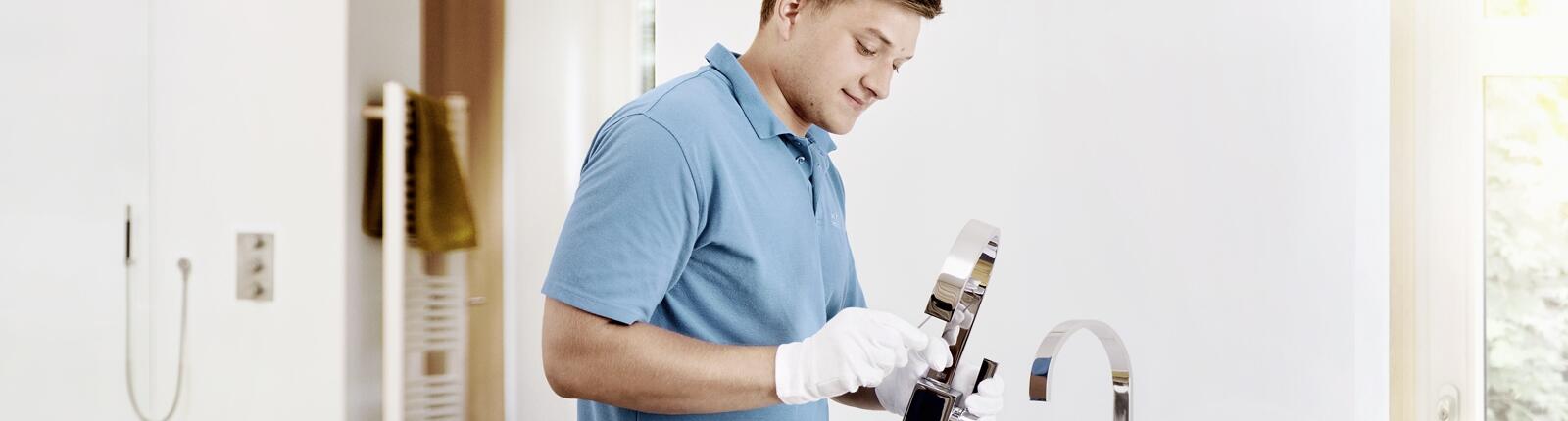 Junger Monteur montiert eine Armatur mit weißen Handschuhen
