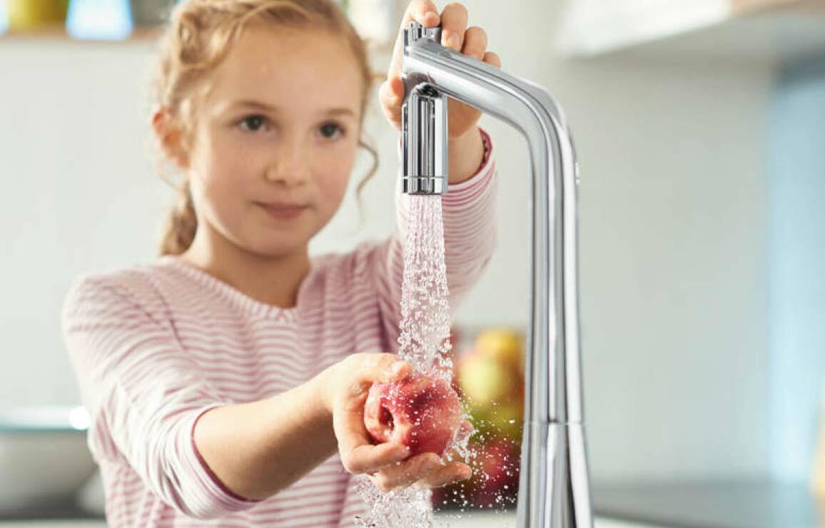 Kind wäscht Obst unter Wasserhahn